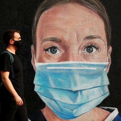 A man wearing a face mask walks by a mural depicting a medical worker in Manchester, Britain on Monday. Photo: Reuters