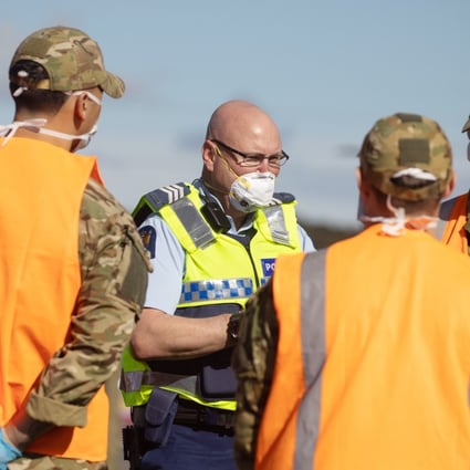 A police officer wearing a protective masks talks to defence force staff at a checkpoint in Auckland. Photo: Bloomberg