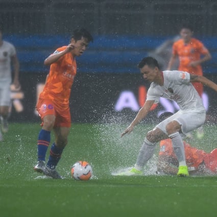Water sprays up from the pitch in the game between Shandong Luneng and Shenzhen in Dalian. Photo: Xinhua