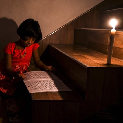 A girl reads a book in candlelight in Colombo. File photo: AFP