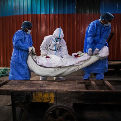 Relatives (in white) along with workers (in blue) wearing PPE help to place the body of a person who died from coronavirus in New Delhi. Photo: AFP