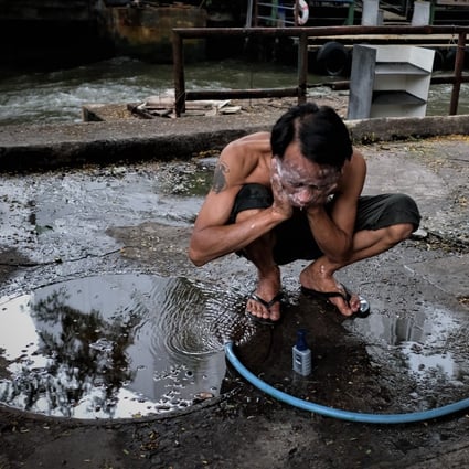 A man washes his face with a hose on the street in Baan Khrua, a shanty town in the centre of Bangkok in the shadow of upscale shopping malls, hotels and condominiums – built where orchards once stood. Photo: Tibor Krausz