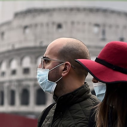 A couple wearing face masks walk past a poster representing the Colosseum in l Rome on Tuesday. Photo: AFP