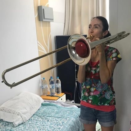 One of the Hong Kong Philharmonic’s quarantined musicians, Megan Sterling, principal flute, plays her husband’s trombone for a change in her quarantine room at Penny’s Bay, Lantau Island. Players have been practising, learning new works, and doing yoga during their confinement. Photo: Megan Sterling