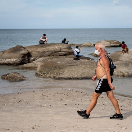 A man wearing a face mask walks along Hua Hin beach in Thailand. Covid-19 is expected to cost the global economy US$20 trillion or more. Photo: AFP