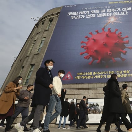 People wearing face masks walk under a banner emphasising an enhanced social distancing campaign in front of Seoul City Hall, South Korea. Photo: AP