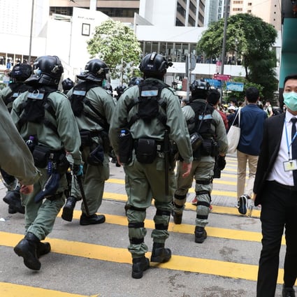 Office workers walk past riot police during an anti-government demonstration in the financial district of Central on May 27, one of several demonstrations held in various locations in Hong Kong that day in protest against the national anthem law and the national security law. The national security law, which took effect an hour before midnight on June 30, has drawn criticism and sanctions from the West, and prompted a rush to emigrate. Photo: Nora Tam