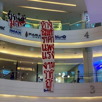 Protesters at Siam Paragon mall unfurling banners. The one on the left proclaims “Abolish Section 112", and the long one next to it reads “Expensive goods from cheap labour”.