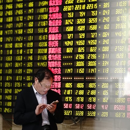 A man looks at his smartphone near a display showing stock prices at a brokerage house in Shanghai. Photo: AP Photo