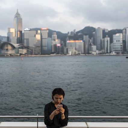 A woman uses a smartphone along Victoria Harbour in the Tsim Sha Tsui on April 29, 2019. Photo: Bloomberg
