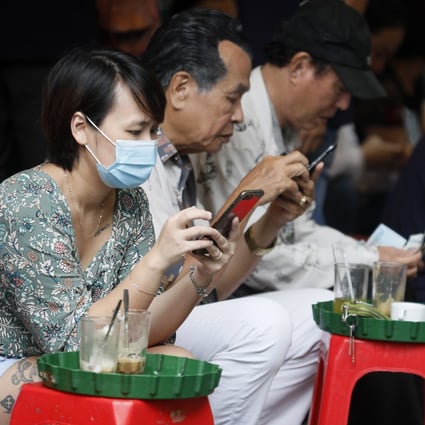 A woman wearing a mask checks her mobile phone at a street cafe in Hanoi. Vietnam has contained the coronavirus faster than much of Asia. Photo: EPA-EFE