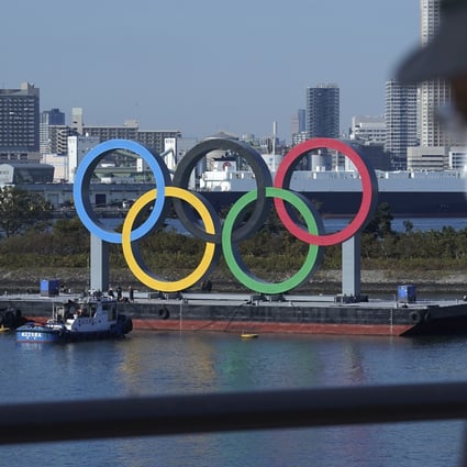 A man wearing a protective face mask to help curb the spread of the coronavirus walks past the Olympic rings in Tokyo. Photo: AP