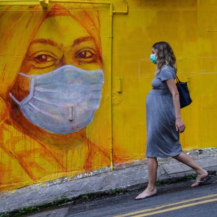 A pregnant woman wearing a face mask walks past a street mural in Hong Kong in March 2020. Photo: AFP