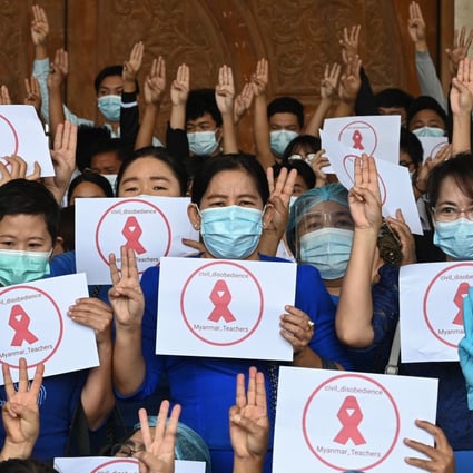 University teachers hold up three-finger salutes and signs with red ribbons calling for civil disobedience during a protest against the military coup at Dagon University in Yangon on Friday. Photo: AFP