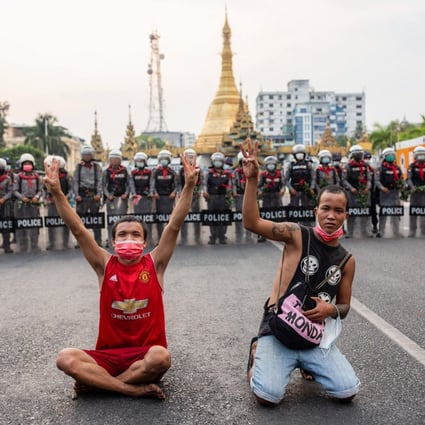 Protesters display the three-fingered salute in front of police officers at the Sule Pagoda. Photo: dpa