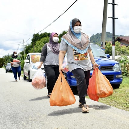 Malaysians carry shopping bags full of supplies as they walk down a deserted road amid the country’s lockdown. Photo: DPA