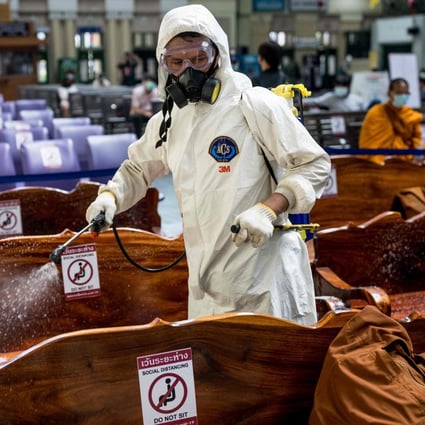 A cleaner wearing personal protective equipment sprays disinfectant on seats in Bangkok’s Hua Lamphong railway station. Photo: AFP