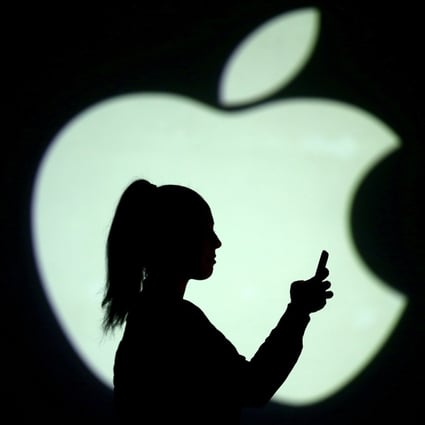 Silhouette of a mobile user seen next to a screen projection of the Apple logo. Photo: Reuters