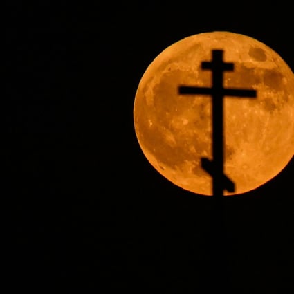 The super blood moon rises over the cross on top of an Orthodox church in the city of Rossosh, Russia on Wednesday. Photo: AFP