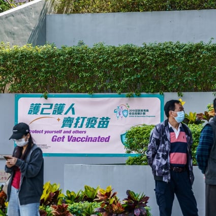 A banner promotes the Covid-19 inoculation programme as people wait outside a community vaccination centre in Hong Kong on March 10. The “wait and see” approach many Hongkongers have taken to vaccination is stalling economic recovery. Photo: Bloomberg