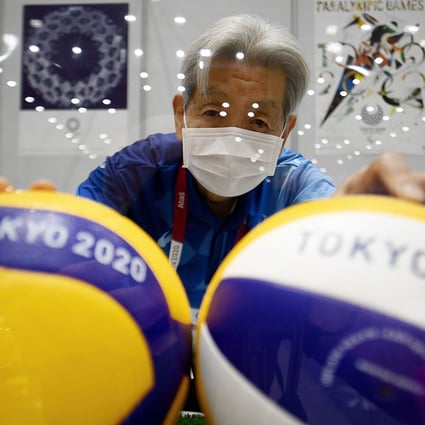 A Tokyo Olympics volunteer wearing a facemask poses with volleyballs behind a protective plexiglass plate at the media centre ahead of the opening of the Tokyo 2020 Olympic Games. Photo: AFP