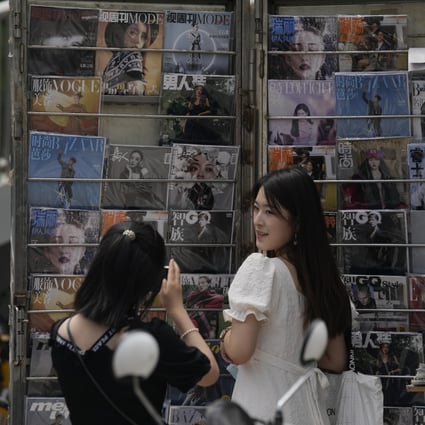 A woman poses for photos near a newsstand with entertainment magazines including one featuring Kris Wu on its cover in Beijing on August 1. Photo: AP
