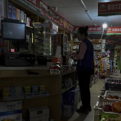 A woman buys groceries from a mini-market using a light bulb powered by a petrol generator during a blackout in Shenyang, Liaoning province, on Wednesday. Photo: AP