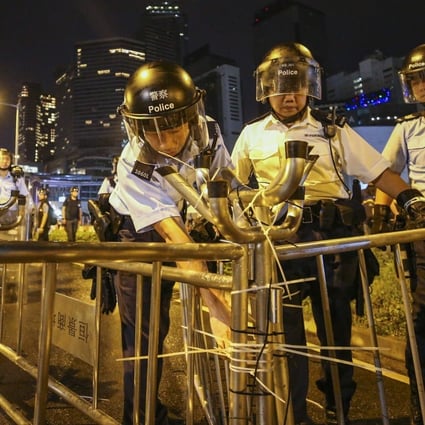 Hong Kong police officers cut zip ties off metal barricades erected by anti-government protesters outside the Legislative Council Complex on July 1, 2019. Photo: Winson Wong