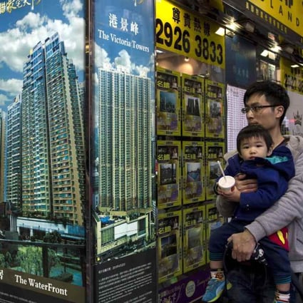 A man carrying a boy walk outside a property agency featuring posters of the latest high-rise apartment buildings in Hong Kong . Photo: Reuters