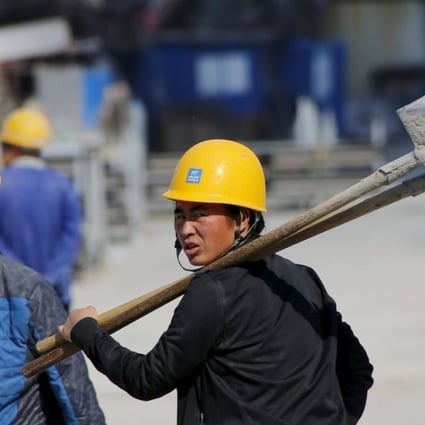 A woman worker, holding shovels, walks past a road construction site in Beijing. Photo: Reuters