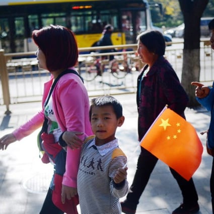 A woman and a child holding up a miniature national flag walk along a road in Beijing as China announced the end of its hugely controversial one-child policy last month after decades of strict, sometimes brutal enforcement left it with an ageing population and shrinking workforce. Photo: AFP