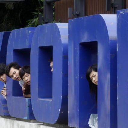 Workers look on from a Foxconn logo near the gate of a Foxconn factory in the township of Longhua, Guangdong province. The once controversial firm is back in favour with job seekers who are faced with a toughening market. Photo: Reuters