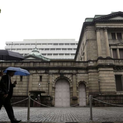 Pedestrians holding umbrellas walk past the Bank of Japan (BOJ) headquarters in Tokyo, Japan, on Thursday, April 28, 2016. The BOJ held off on expanding monetary stimulus at its monthly meeting in April, as Governor Haruhiko Kuroda and his colleagues opted to take more time to assess the impact of negative interest rates. Photographer: Bloomberg
