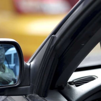 A driver is reflected in a side mirror as he uses the Didi Chuxing car-hailing application. Photo: Reuters