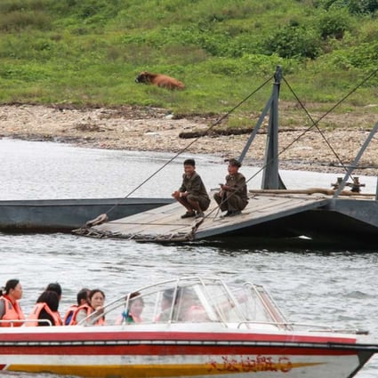 Two North Korean soldiers look at Chinese tourists taking a boat ride along an inner river in North Korea. Photo: Simon Song
