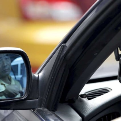 A taxi driver is reflected in a side mirror as he uses the Didi Chuxing car-hailing application in Beijing. Driver subsidies in some mainland cities are being reduced since the Uber China buyout. Photo: Reuters