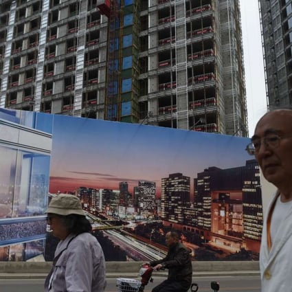 People walk past a billboard advertising a new housing complex outside a construction site in Beijing. Some developers are desperate to acquire land in the nation’s capital. Photo: AFP