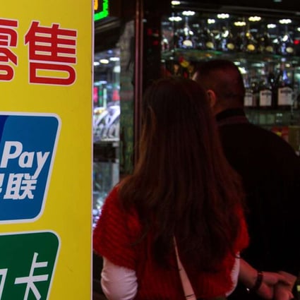 Chinese visitors walk past a sign for China UnionPay outside a pawnshop in Macau. Curbs on taking out cash in the former Portuguese enclave mark the latest move to curb the flow of money out of the mainland. Photo: Reuters