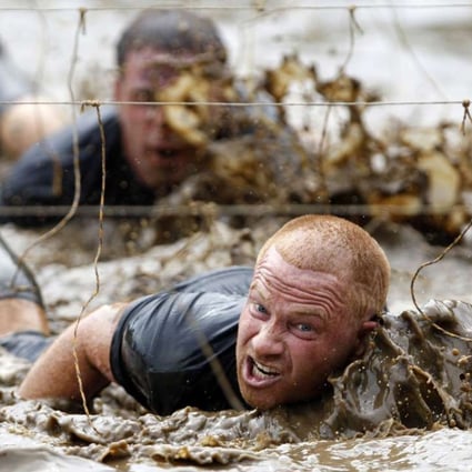 Competitors swim through mud underneath electrified wires during a Tough Mudder. Photo: Reuters