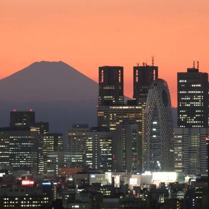 Mount Fuji, Japan's highest mountain, towers behind skyscrapers in Tokyo's Shinjuku area during sunset.