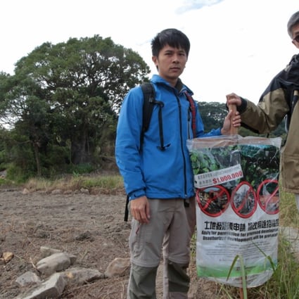 Conservationists Roy Ng Hei-man and Michael Lau Wai-neng beside a government banner on enclaves destruction in Sha Lo Tung, Tai Po. Photo: Bruce Yan