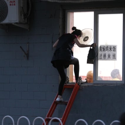 A woman climbs a ladder to enter a small Beijing restaurant via a window on May 10. Photo: Simon Song