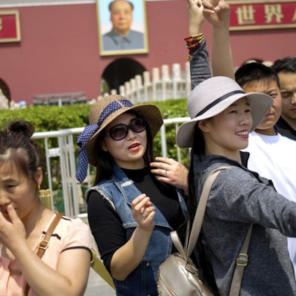 Women gesture as they pose for a photo in front of Tiananmen Gate during the May Day holiday in Beijing. A survey showed that Chinese are choosing work rather than have children. Photo: AP