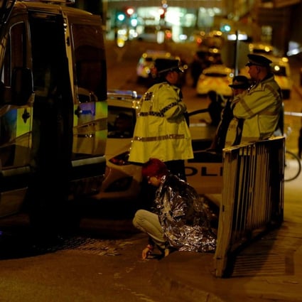 A woman sits in the street in a blanket near the Manchester Arena as police guard the area following an explosion on Monday night. Photo: EPA