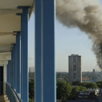 A resident in a nearby building watches smoke rise from a building on fire in London. Photo: AP