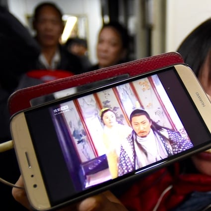 A passenger watches a programme on her mobile phone during a train journey. Xinhua