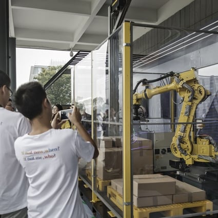 Employees and visitors take photographs of logistic and parcel delivery robots on display at the Alibaba Group headquarters in Hangzhou, China, on Friday, Sept. 8, 2017. Photo: Bloomberg