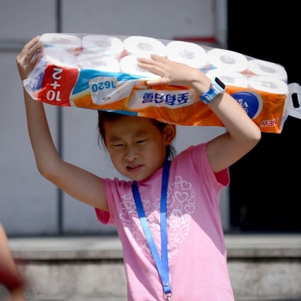 Stocking up: A girl walks out of a Beijing supermarket on August 9, 2016 with a bundle of toilet paper rolls. Photo: AFP