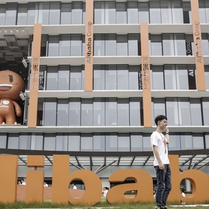 Employees and visitors pose for a photograph in front of signage for Alibaba Group Holding Ltd. at the company's headquarters in Hangzhou, China. Photo: Bloomberg