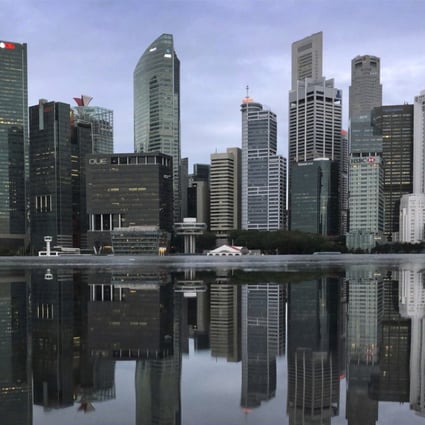The financial skyline of Singapore is reflected in a rain puddle as people jog past at dawn in Singapore. Photo: AP